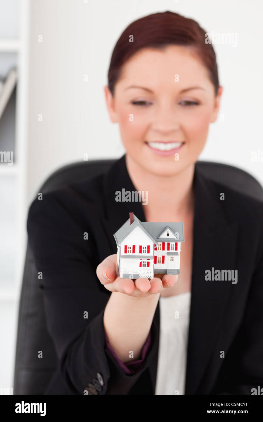 Beautiful red-haired woman in suit holding a miniature house Banque D'Images