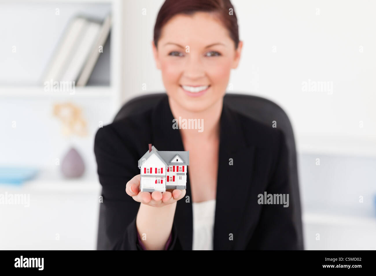 Joli red-haired woman in suit holding a miniature house Banque D'Images
