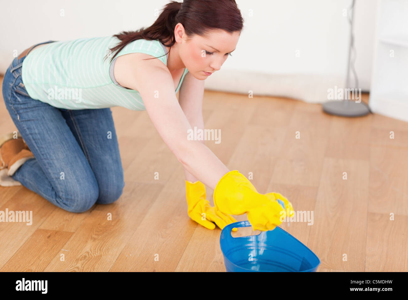 Red-haired woman nettoyage du plancher tout en s'agenouillant Banque D'Images