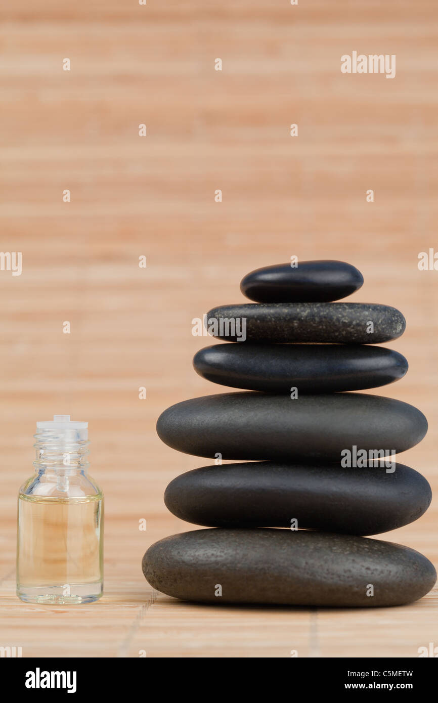 Flacon en verre rempli de liquide jaune pâle et une pile de cailloux noirs Banque D'Images