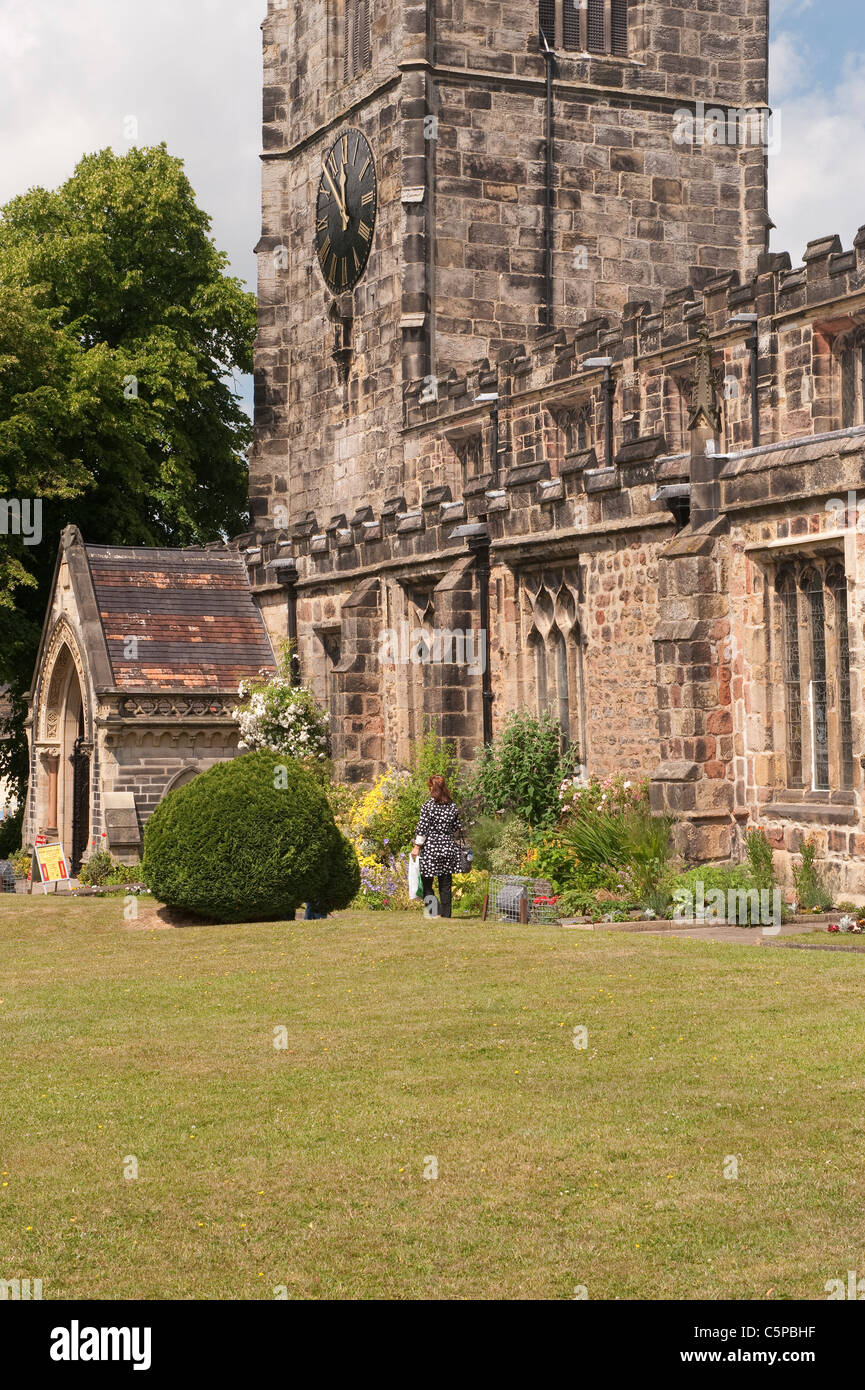 Église Sainte-Trinité, Skipton - 1 femme marchant dans un beau jardin de chantier ensoleillé près du porche sud et tour d'horloge en pierre - North Yorkshire, Angleterre, Royaume-Uni. Banque D'Images