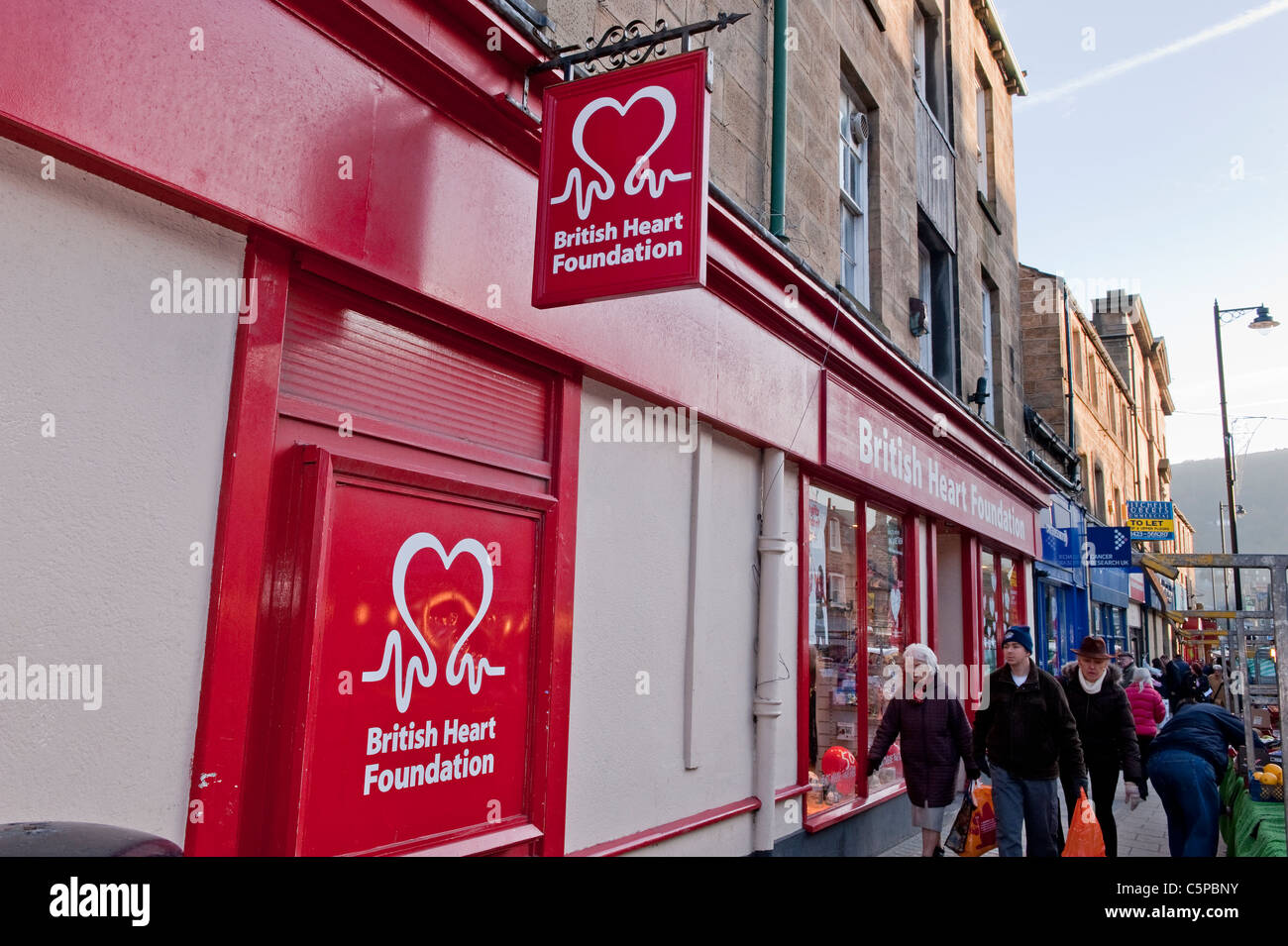 Très fréquentée, la journée du marché (personnes transportant des sacs de shopping, des magasins et logo de la British Heart Foundation Charity Shop - Otley, West Yorkshire, Angleterre). Banque D'Images