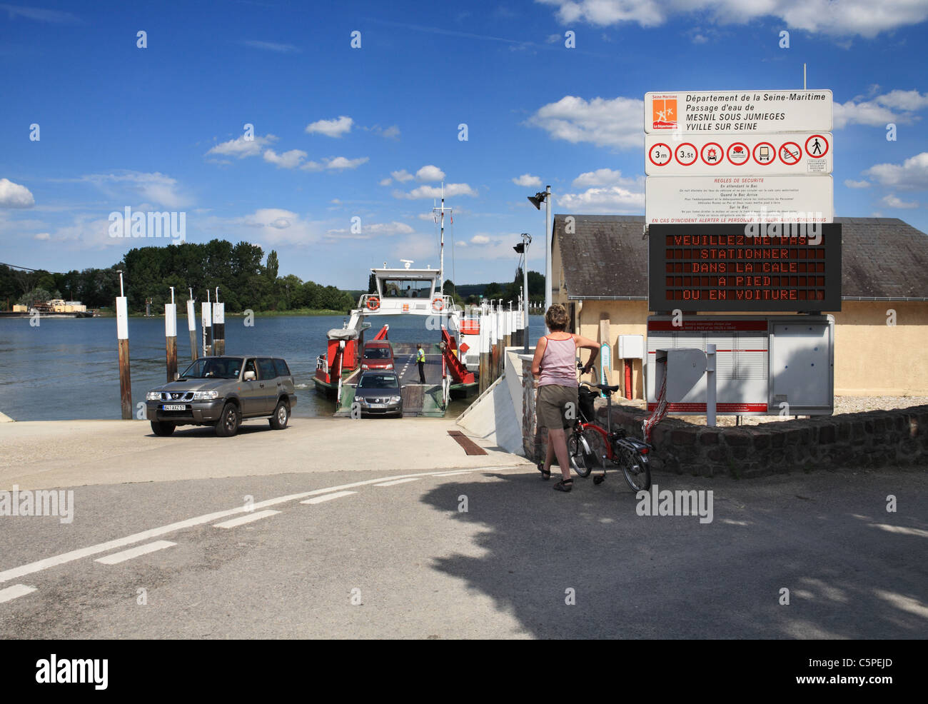 Un car-ferry sur le fleuve Seine décharge alors qu'un cycliste féminin attend d'office. Près de Jumièges, Normandie, France Banque D'Images