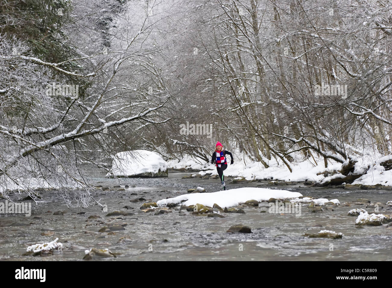 Un jogger traversant une rivière alpine enneigé Banque D'Images