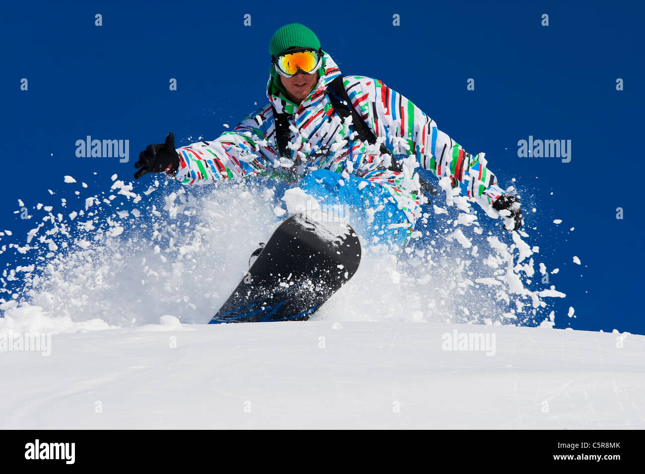 Un snowboarder riding disque à travers la poudreuse fraîche sourit. Banque D'Images