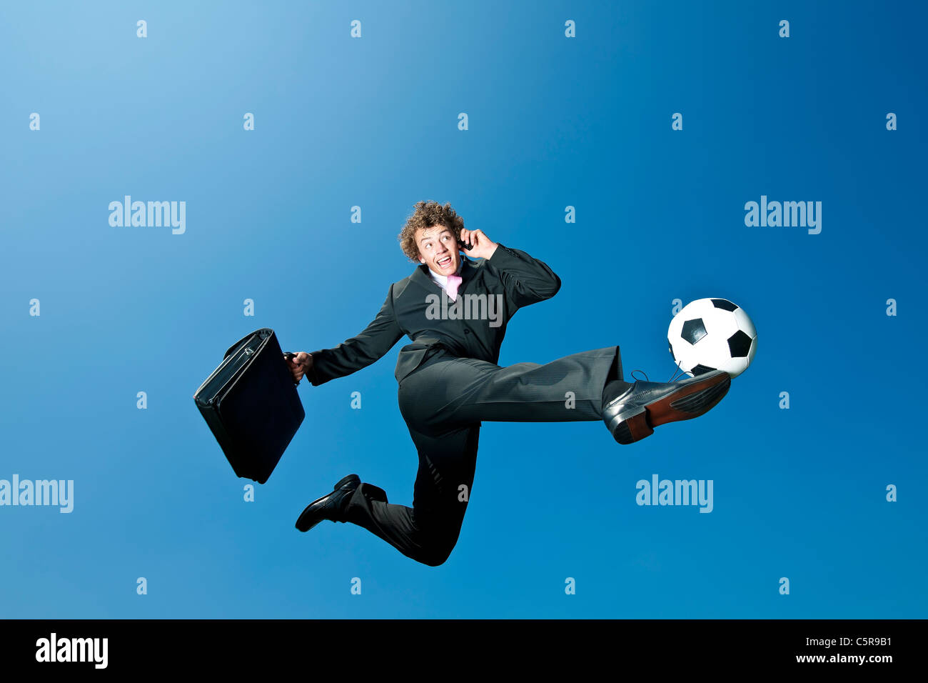 Un homme d'affaires de soccer kicks la balle alors que sur téléphone portable. Banque D'Images