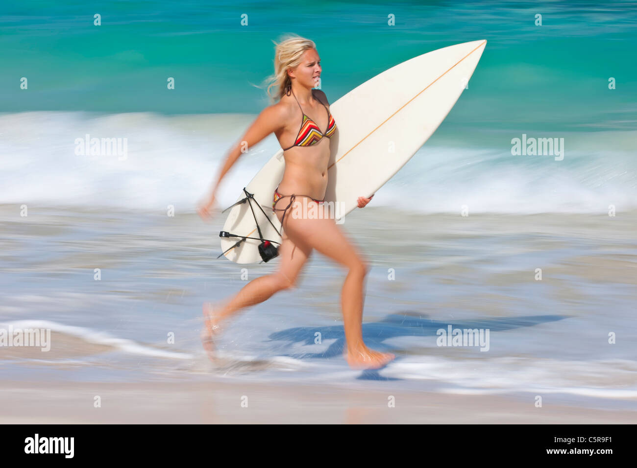 Un jeune surfeur blond court le long du bord de l'océan avec planche de surf. Banque D'Images