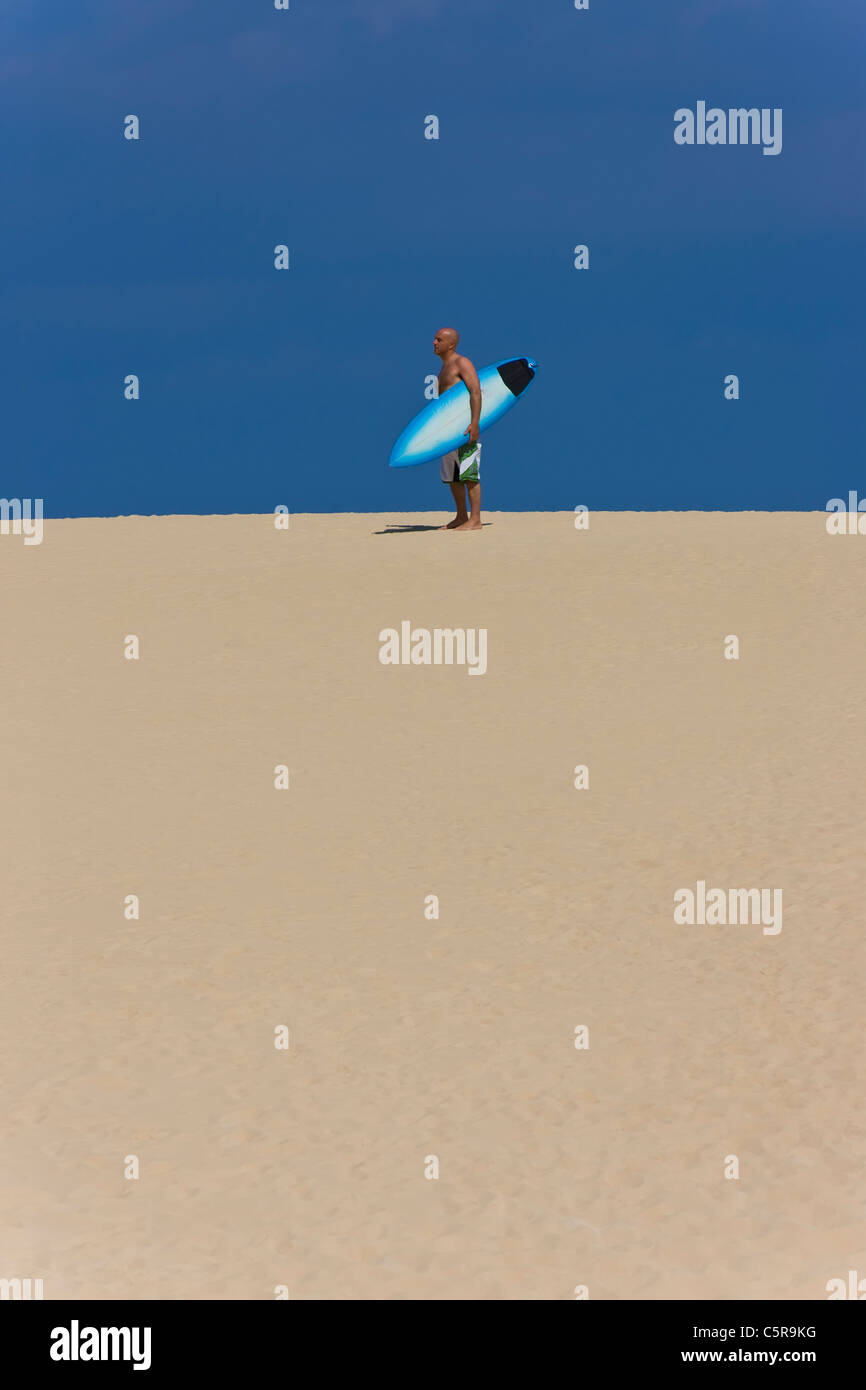 Un surfeur debout sur une dune de sable avec surf. Banque D'Images