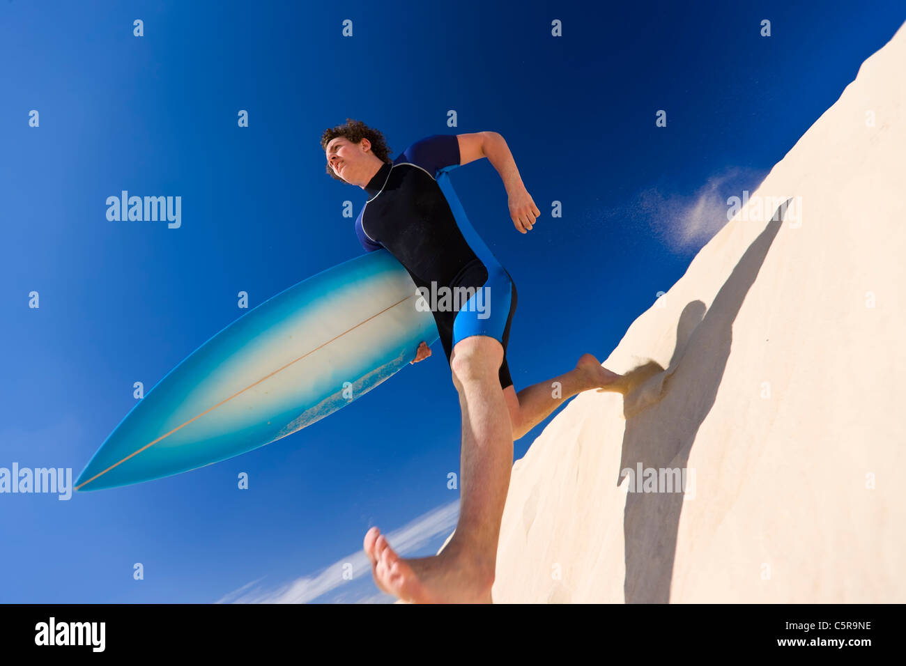 Surfer en prenant de grands progrès vers le bas dune de sable pour l'océan. Banque D'Images