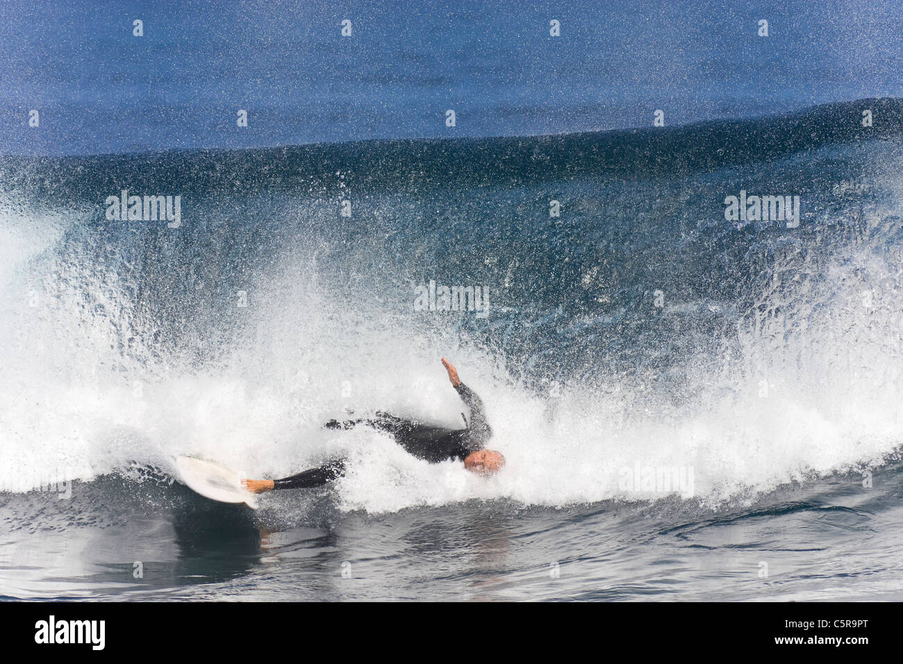 Grosse Vague s'écrase sur le surfer qui a encore un pied sur la planche de surf. Banque D'Images