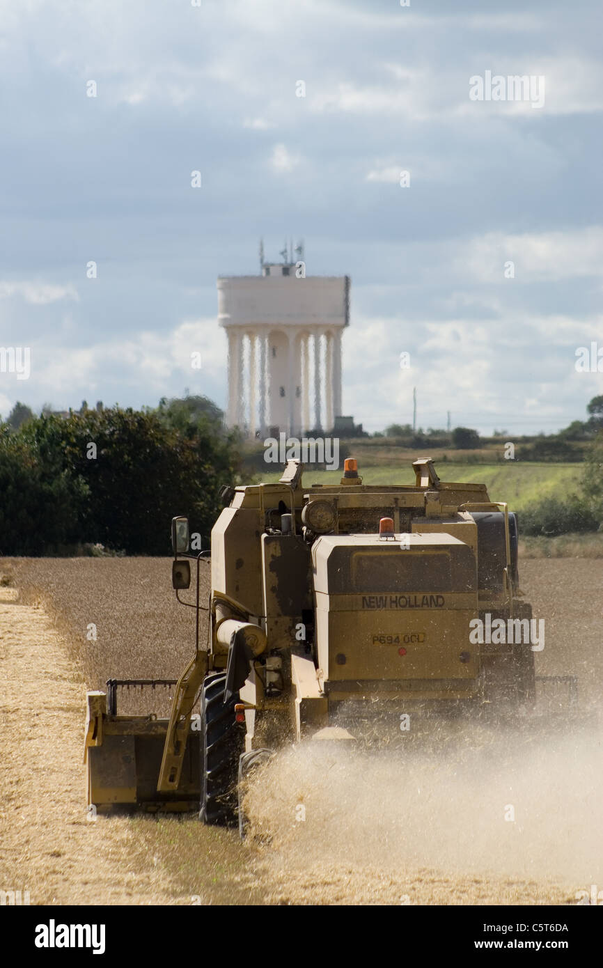 New Holland TX65 Moissonneuse-batteuse, la récolte du blé dans la région de North Norfolk avec le château d'eau à Hill soixante au loin. Banque D'Images