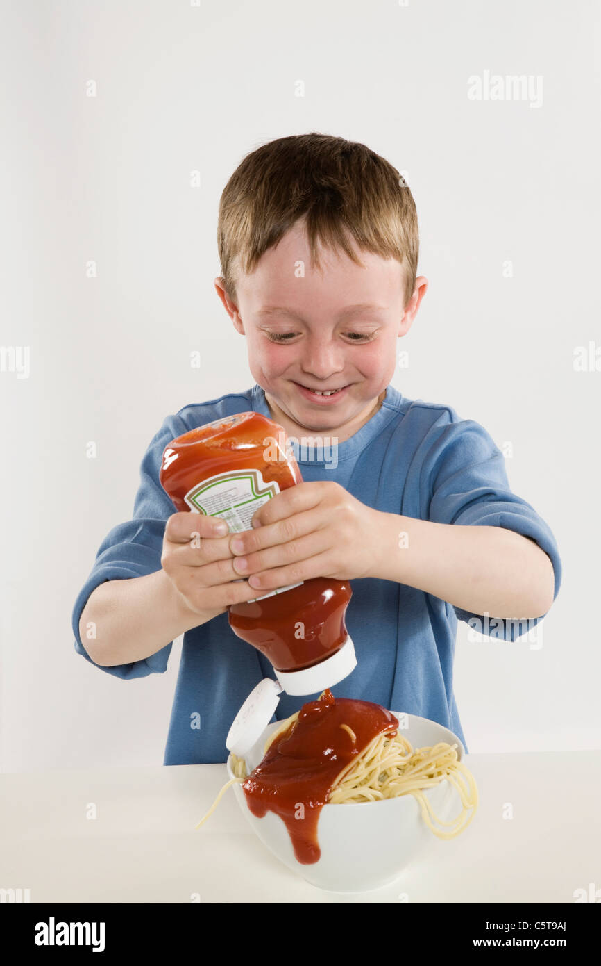 Boy (6-7) pouring ketchup sur les spaghettis Banque D'Images