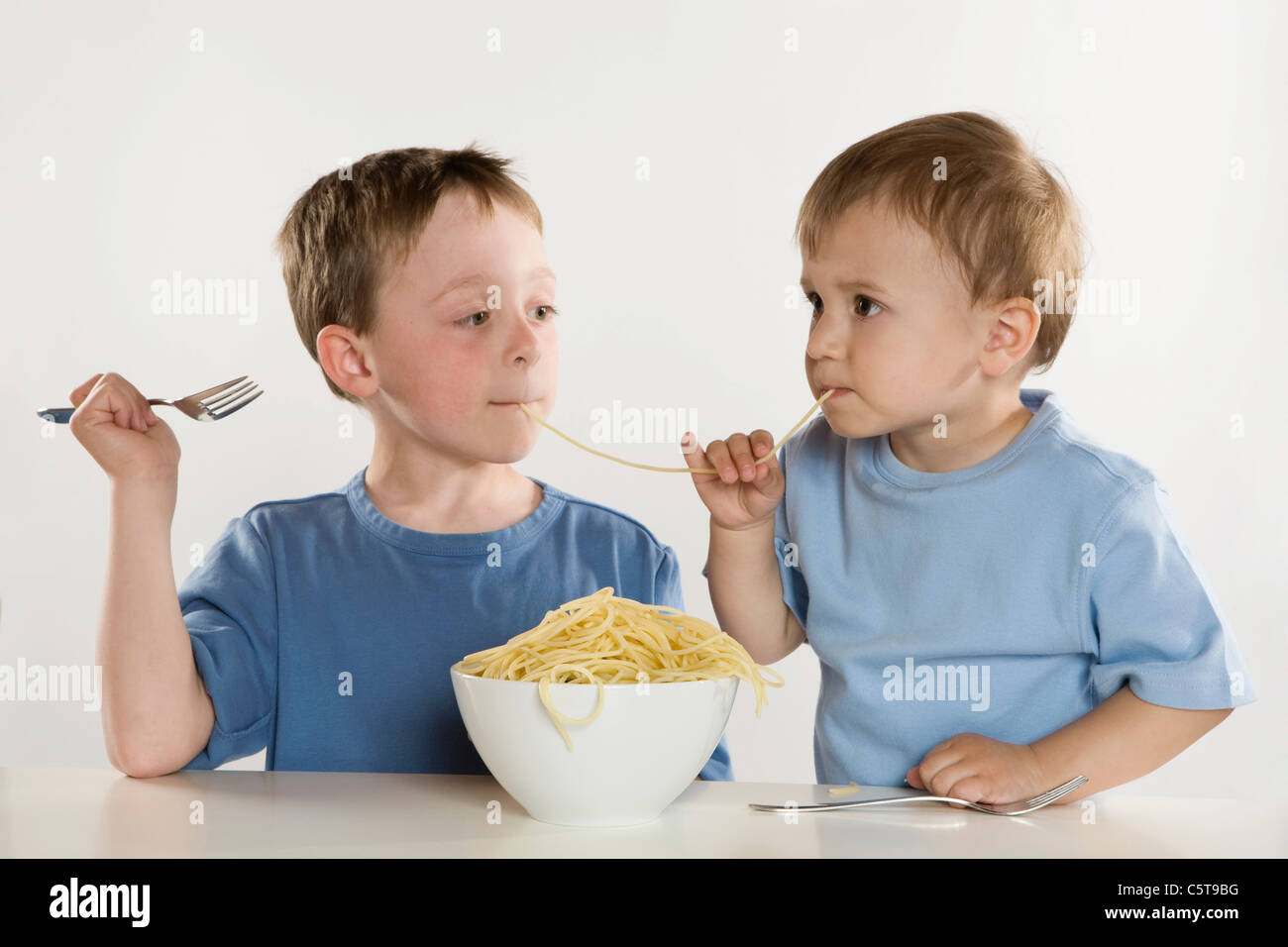 Deux garçons (6-7) (2-3) eating spaghetti, partageant les nouilles, portrait Banque D'Images