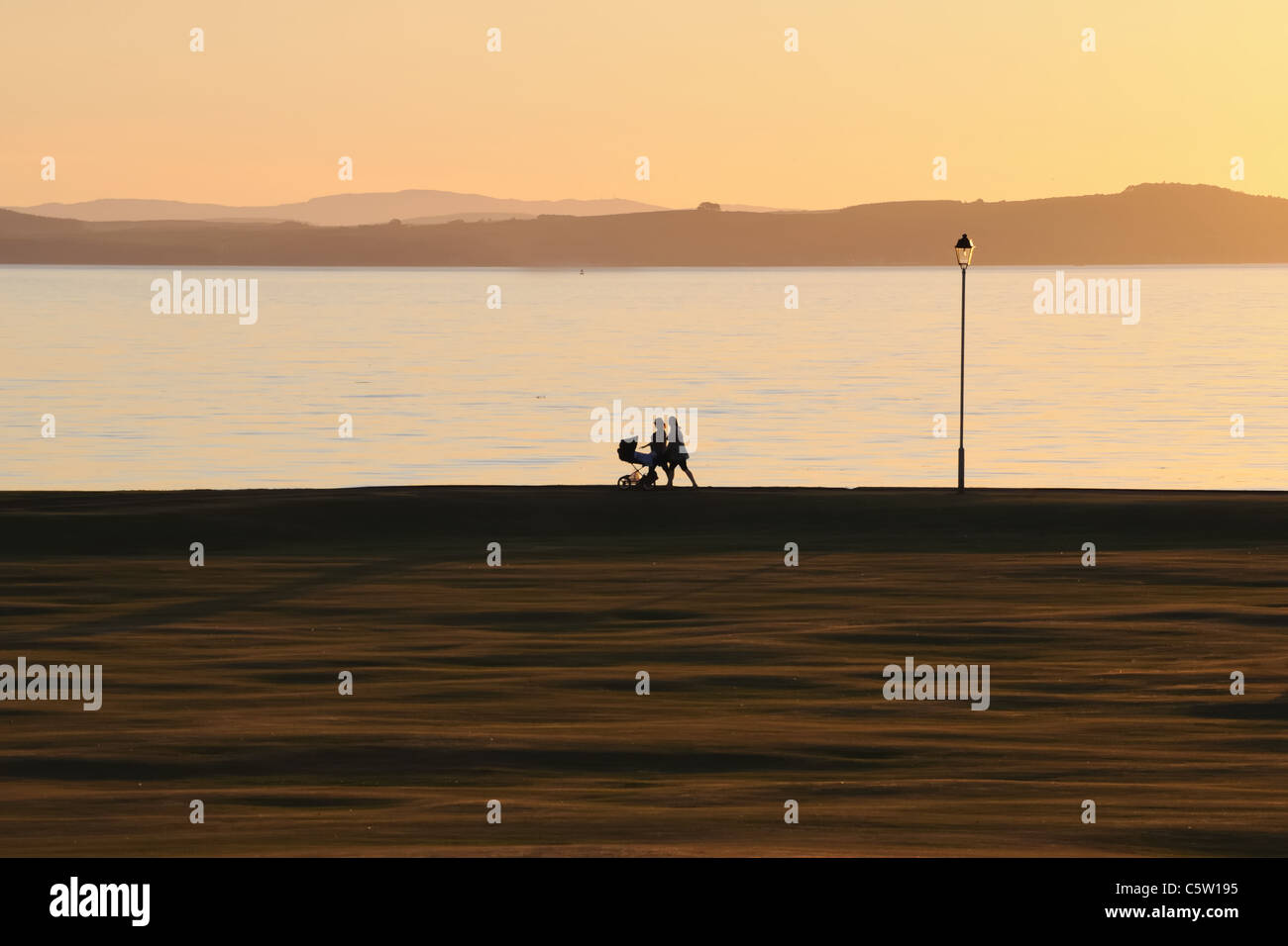 Silhouette de femmes poussant le pram au coucher du soleil sur le front de mer à Largs, Ayrshire, Écosse, Royaume-Uni Banque D'Images