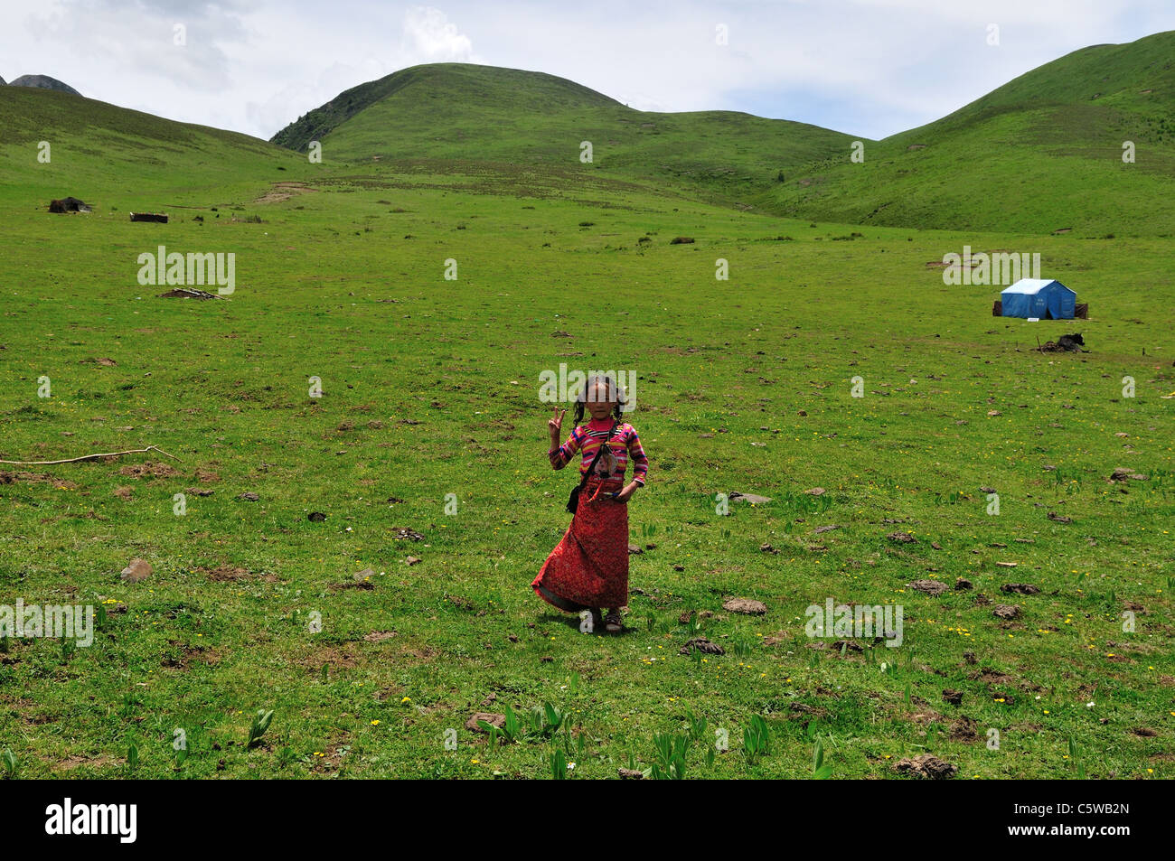 Une jeune fille tibétaine en jupe rouge vagues sa main. Au Sichuan, en Chine. Banque D'Images