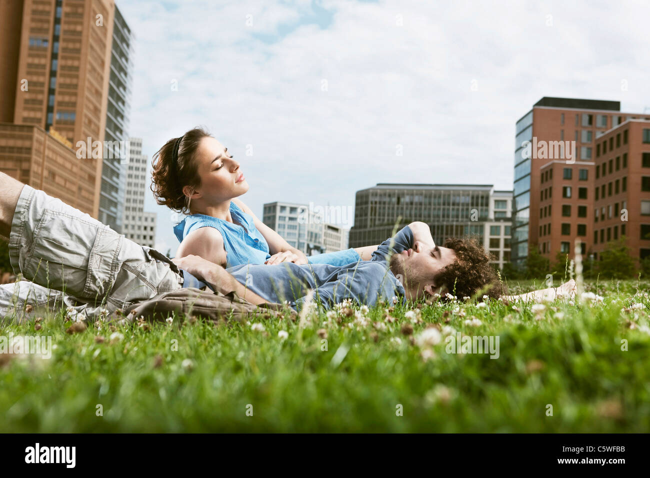 Allemagne, Berlin, Young couple lying in meadow, immeubles de grande hauteur en arrière-plan Banque D'Images