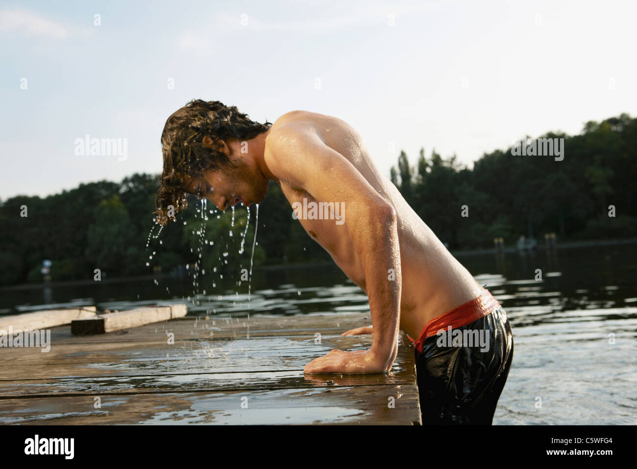 Allemagne, Berlin, Young man climbing on Jetty, side view Banque D'Images