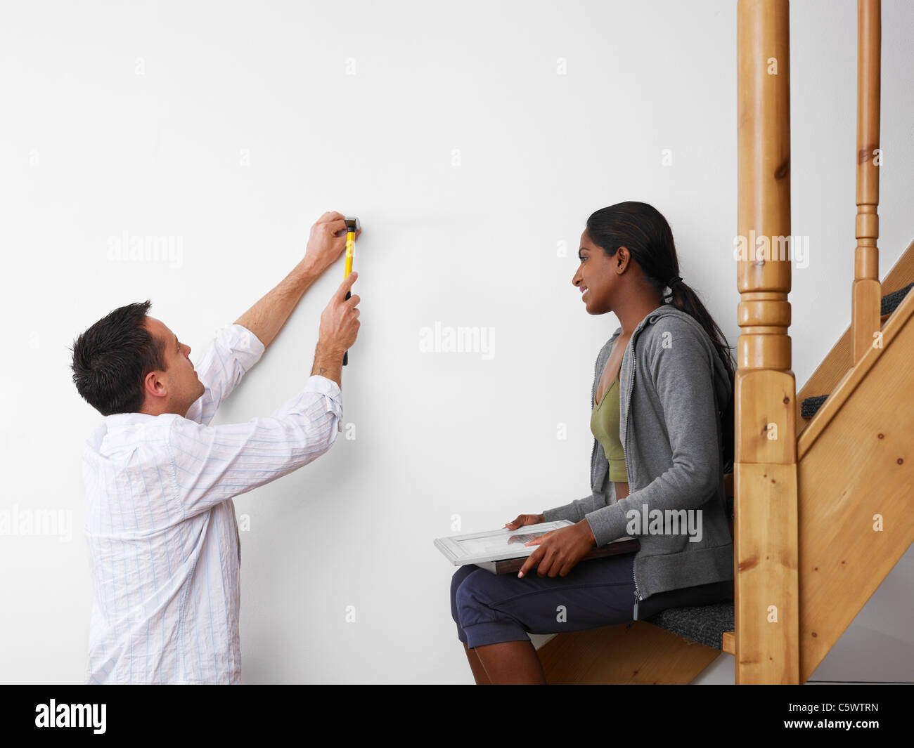 Young couple multiethnique à l'aide d'un marteau pour accrocher des photos sur le mur et sourit. Copy space Banque D'Images