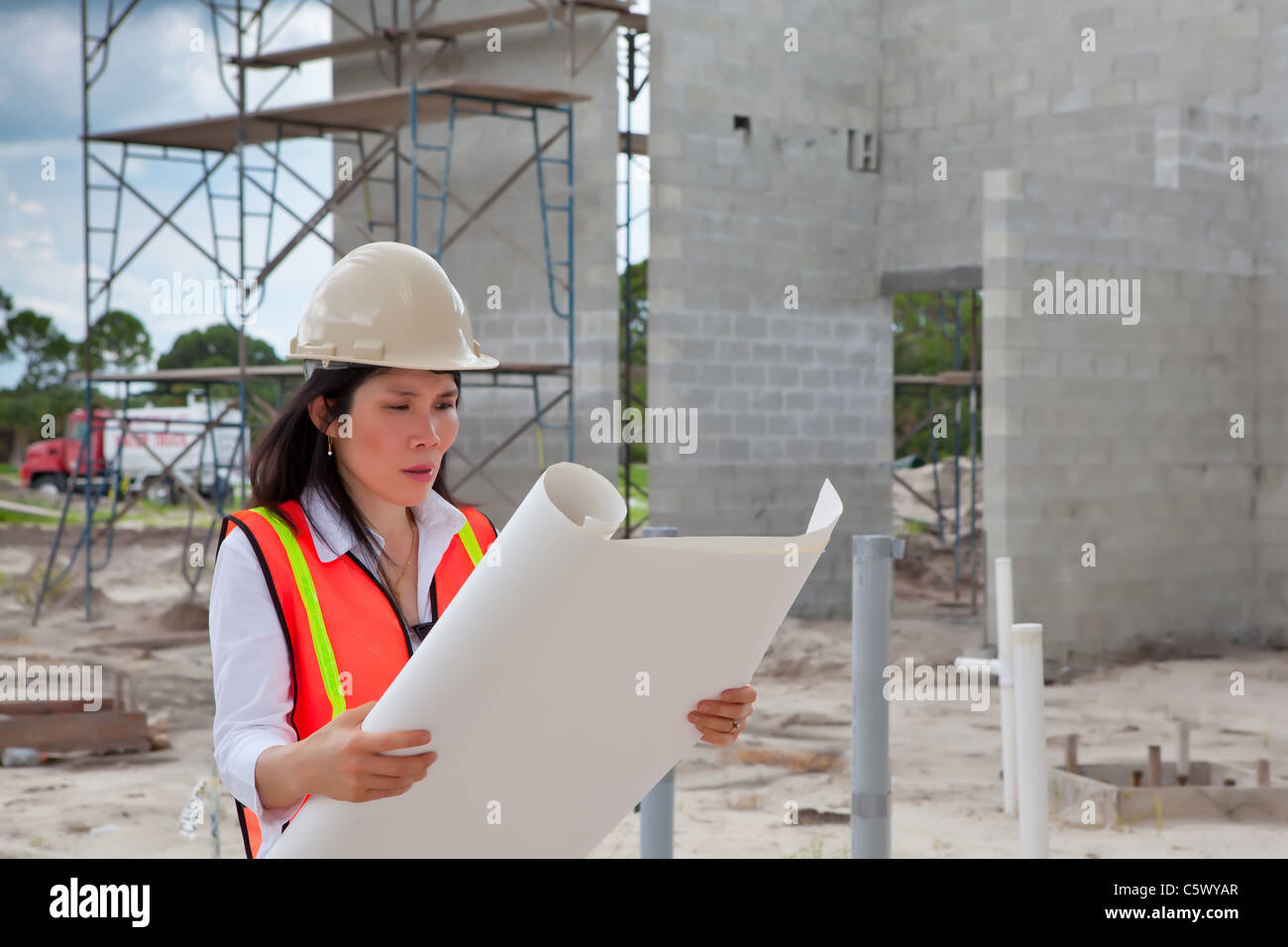 Femme Asiatique Inspecteur sur chantier de construction. Les échafaudages, camion, tuyaux de plomberie et des murs de l'édifice en arrière-plan. Banque D'Images