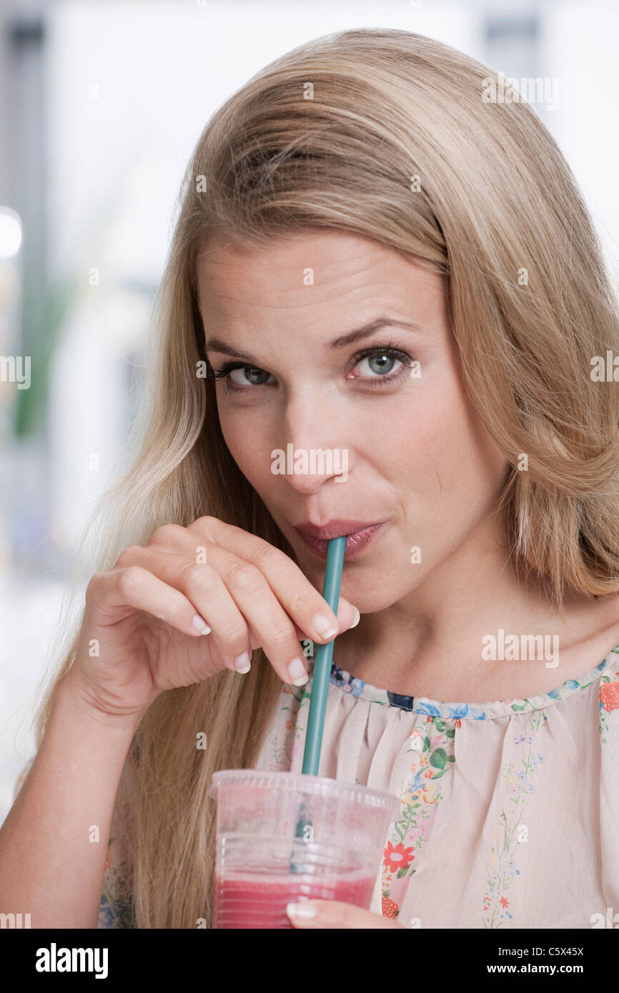 Germany, Cologne, young woman drinking à travers la paille, portrait, close-up Banque D'Images