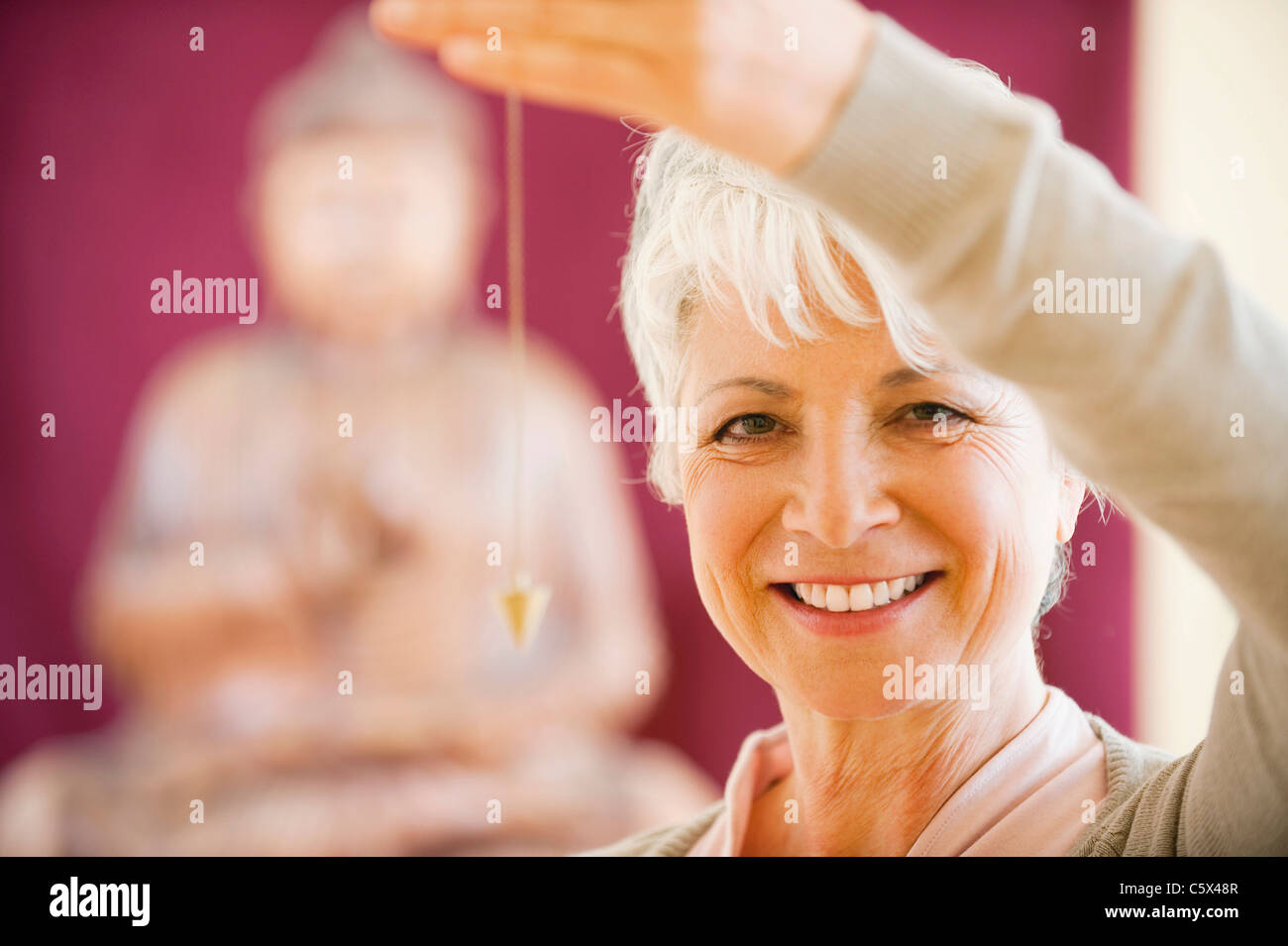 Senior woman holding pendulum, smiling, portrait Banque D'Images