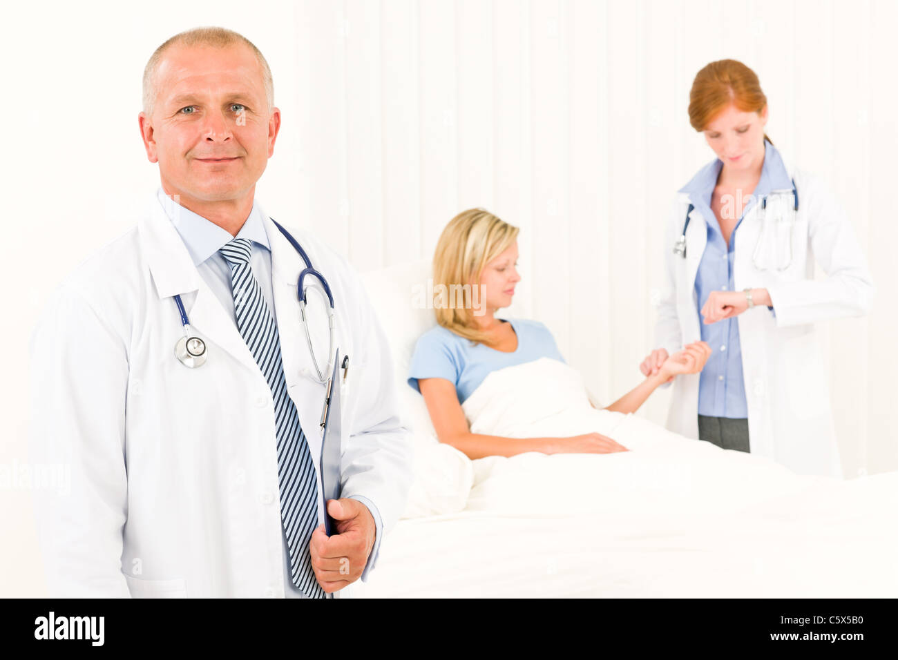 Deux médecins avec patient Lying in Bed examiner pulse Banque D'Images