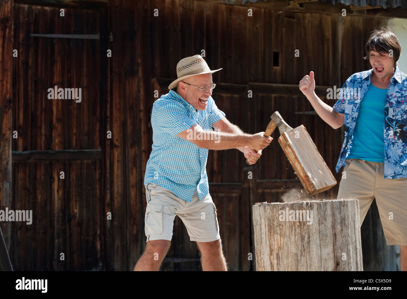 Germany, Bavaria, Senior man chopping wood, man in background cheering Banque D'Images