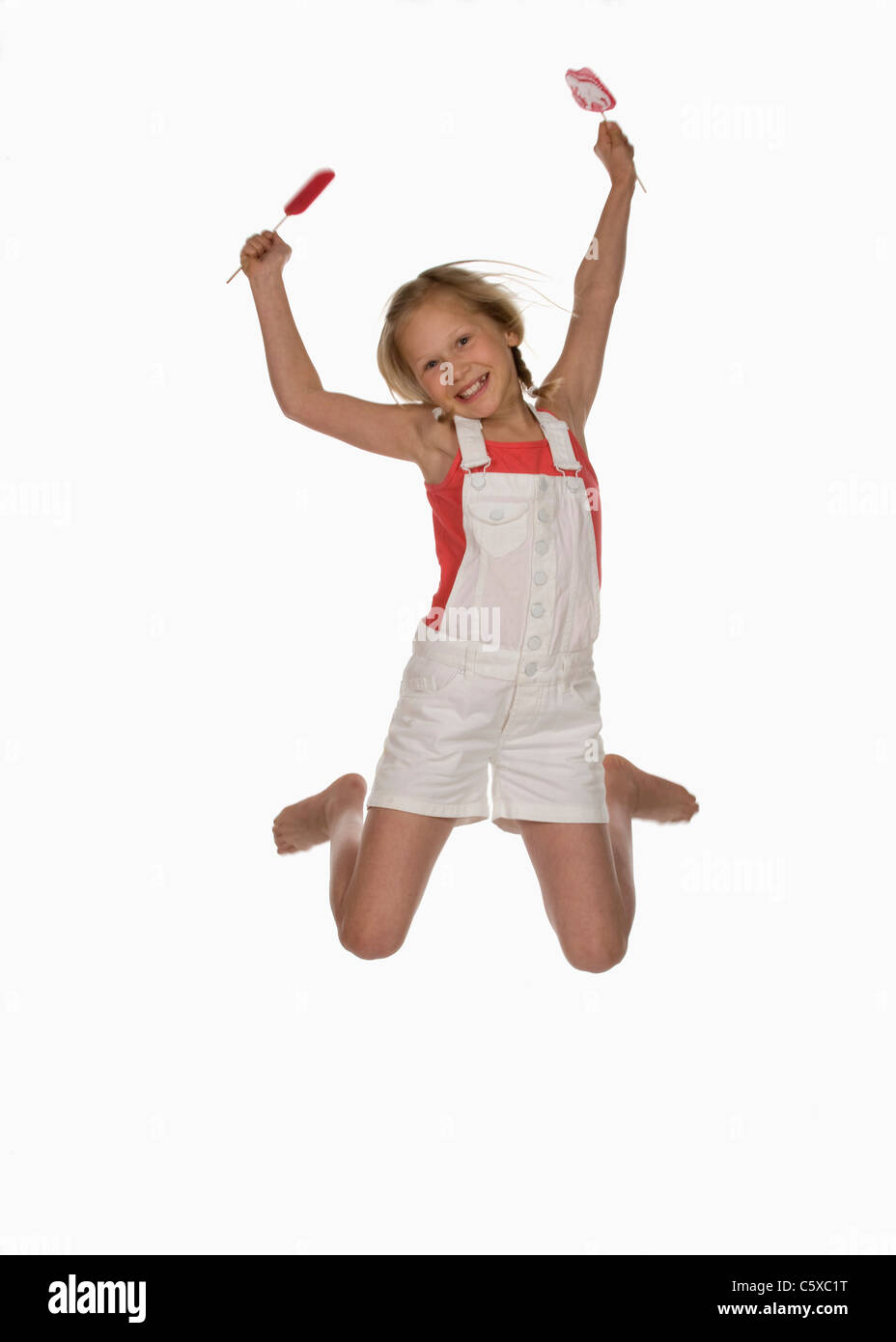 Girl (10-11) holding lollypops, sauter dans l'air, smiling, portrait Banque D'Images