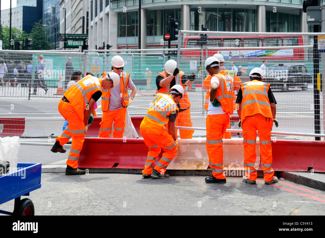 Vêtements haute visibilité casque et travail d'équipe de nombreuses mains travaillent ensemble sept ouvriers mettent des panneaux de clôture en acier sur les travaux routiers dans Victoria Londres Angleterre Royaume-Uni Banque D'Images