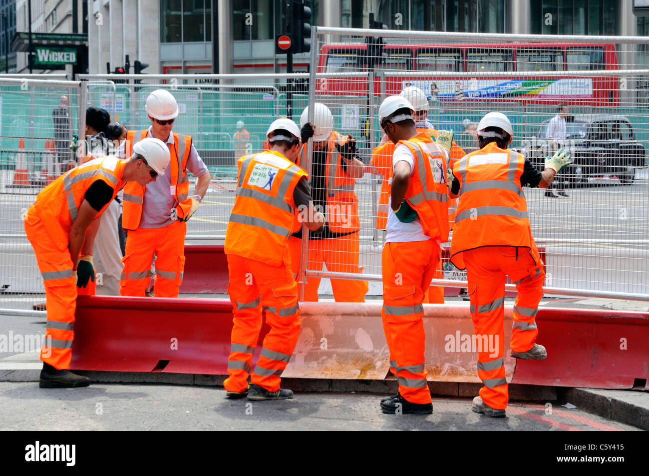 Vestes haute visibilité avec casque de sécurité et le travail d'équipe travailler ensemble par sept ouvriers mettre des panneaux clôtures en acier de l'autre côté de la rue pour Street London England UK fonctionne Banque D'Images