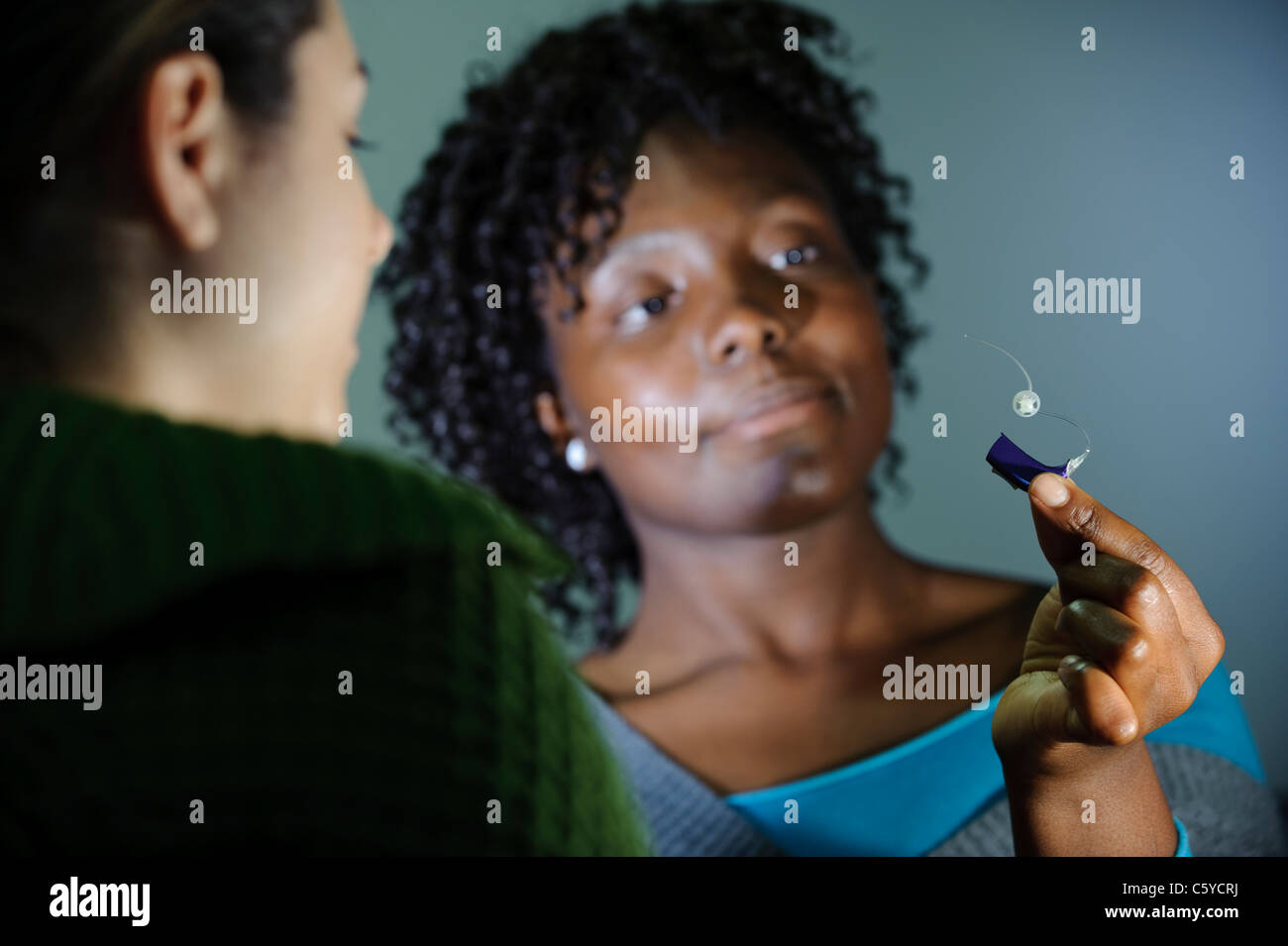 L'audiologie et la surdité femelle student holding up une petite aide auditive montrant à un autre étudiant d'audiologie Banque D'Images