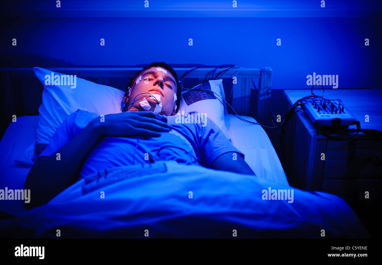 Young male patient 18-20 en laboratoire du sommeil avec l'étude d'équipement d'EEG et d'électrodes sur la tête. Prix allumé en bleu Banque D'Images