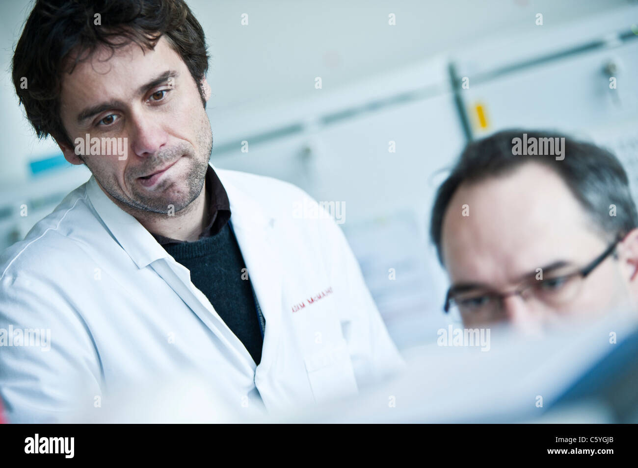 Scientifiques masculins en sarraus de laboratoire à la recherche de données sur l'écran de l'ordinateur en laboratoire. Sur le côté gauche à la question scientifique Banque D'Images