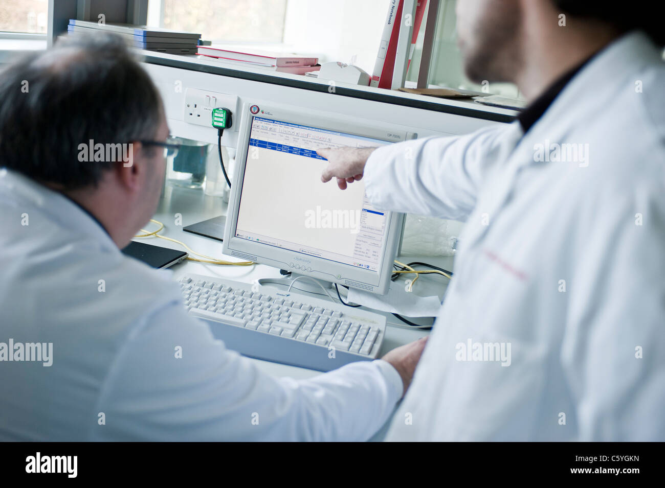 Scientifiques masculins en sarraus de laboratoire à la recherche de données scientifiques sur l'écran de l'ordinateur in laboratory Banque D'Images