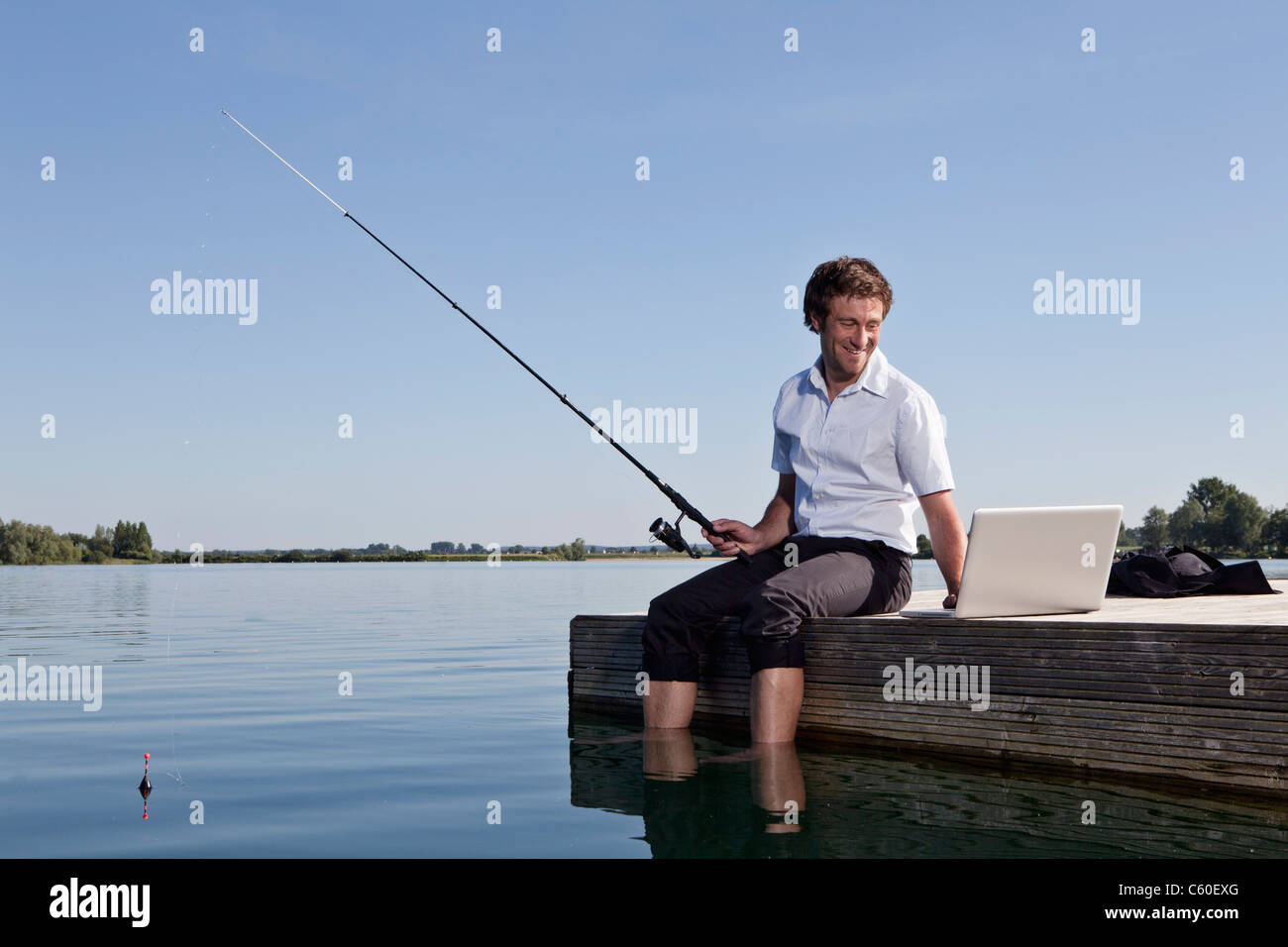 L'homme et la pêche à l'aide de l'ordinateur portable sur dock Banque D'Images