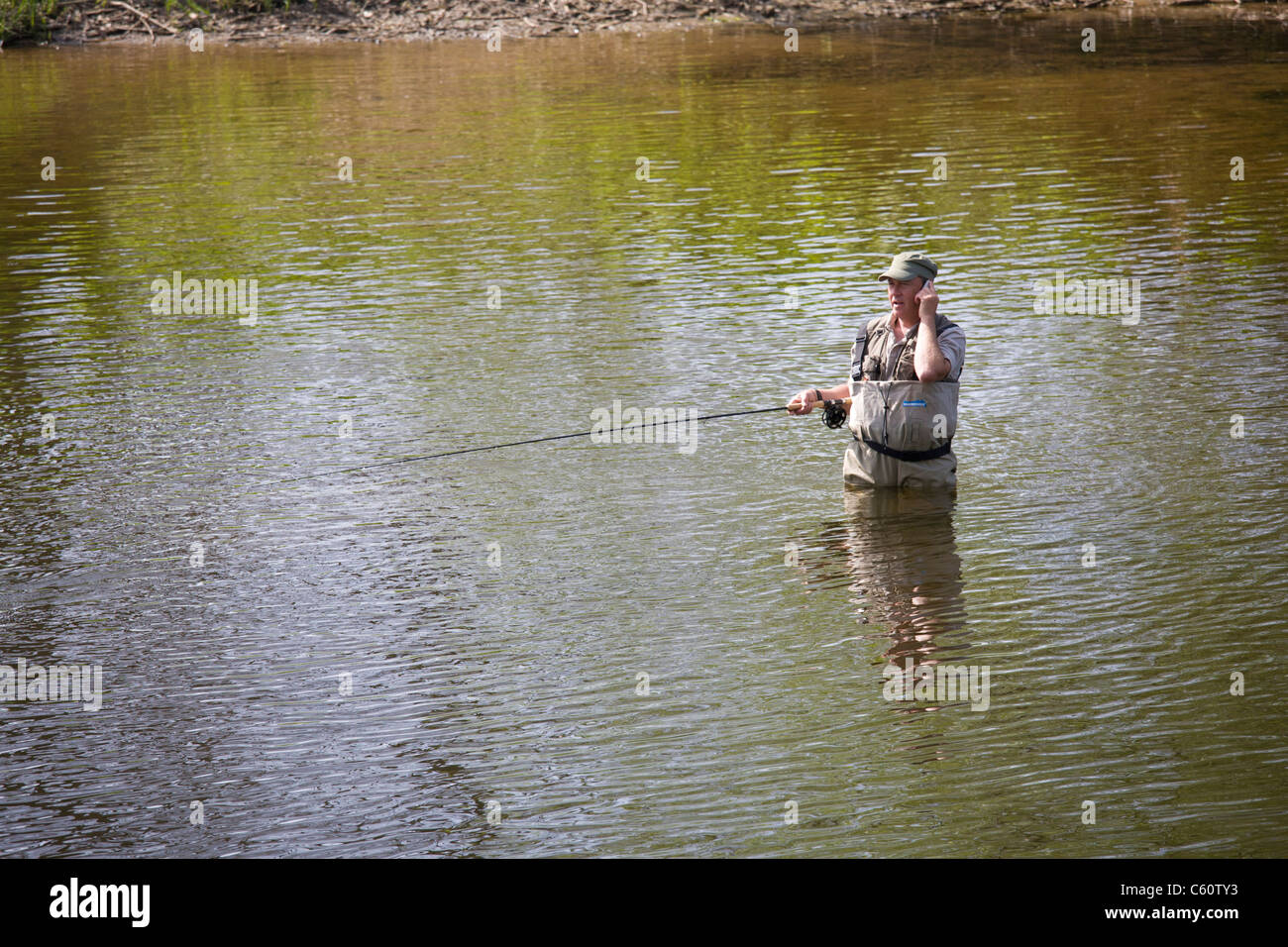 L'homme pêche en rivière tout en faisant un appel de téléphone mobile. Banque D'Images