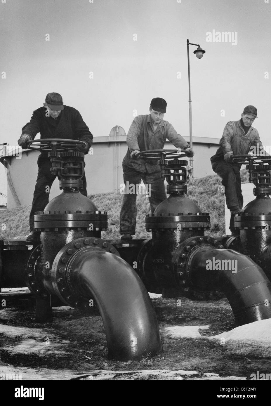 Les hommes tournent les roues de grandes vannes qui régulent le flux d'huile dans des pétroliers à un port de la côte atlantique des États-Unis. Ca. 1944. Banque D'Images