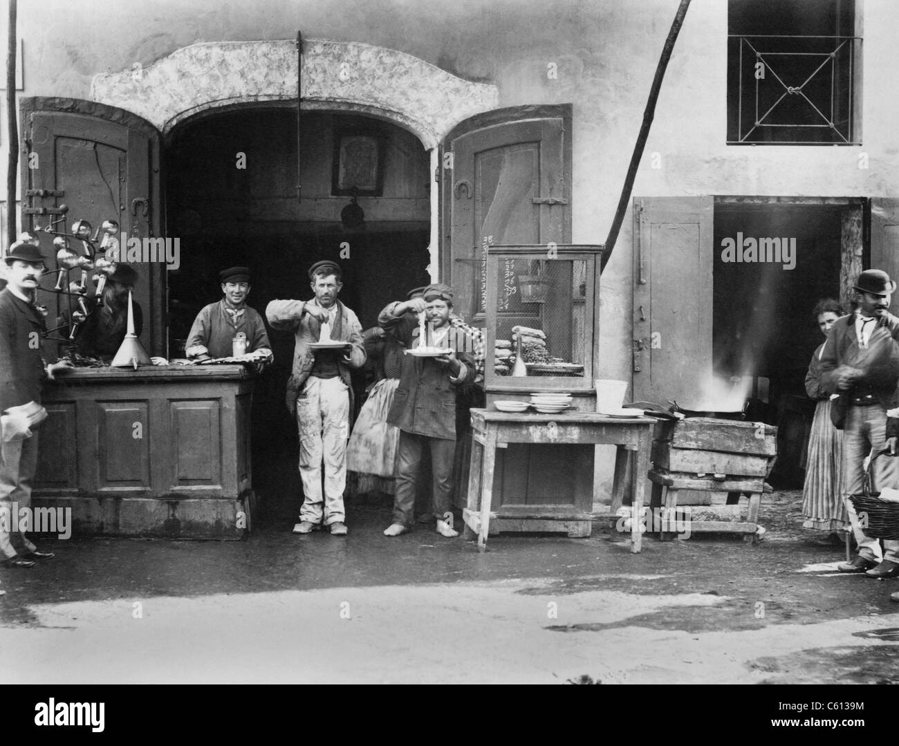 Deux hommes avec des assiettes de spaghetti long mangent au restaurant de la rue de Naples, Italie. Ca. 1900. Banque D'Images