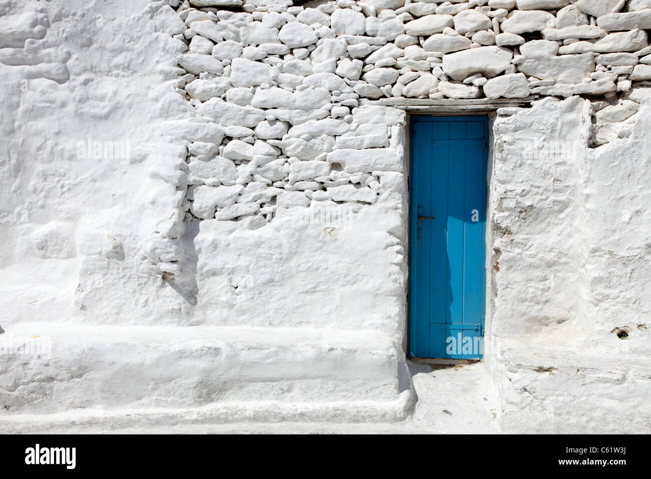 Porte en bois bleu étroit dans un mur en brique blanche. Vieille ville de Mykonos, Grèce, Europe. Banque D'Images