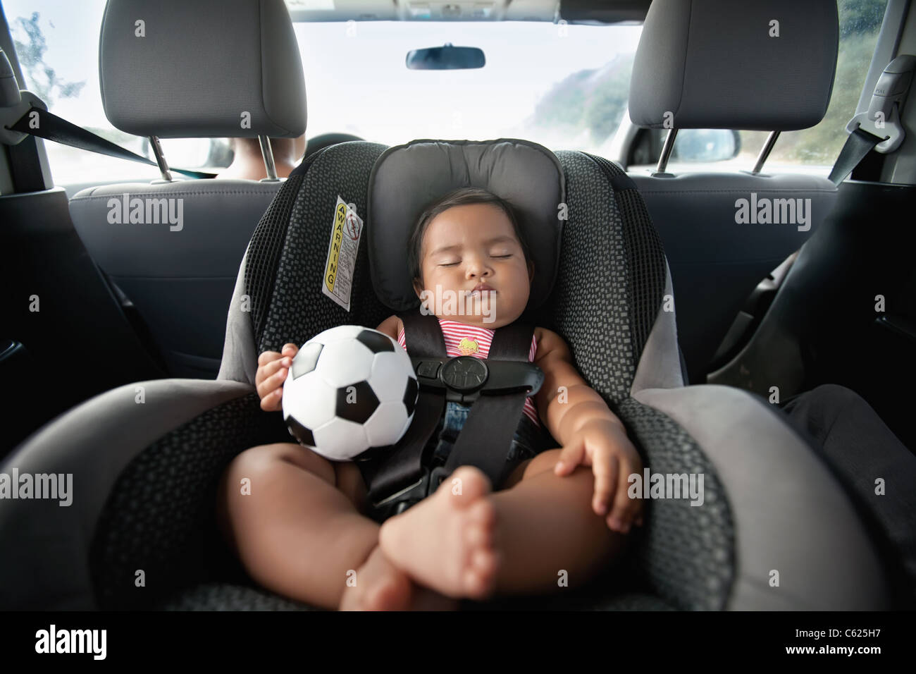 Baby sleeping in car seat et tenant un ballon de football en utilisant l'arrière siège bébé pour la sécurité Banque D'Images