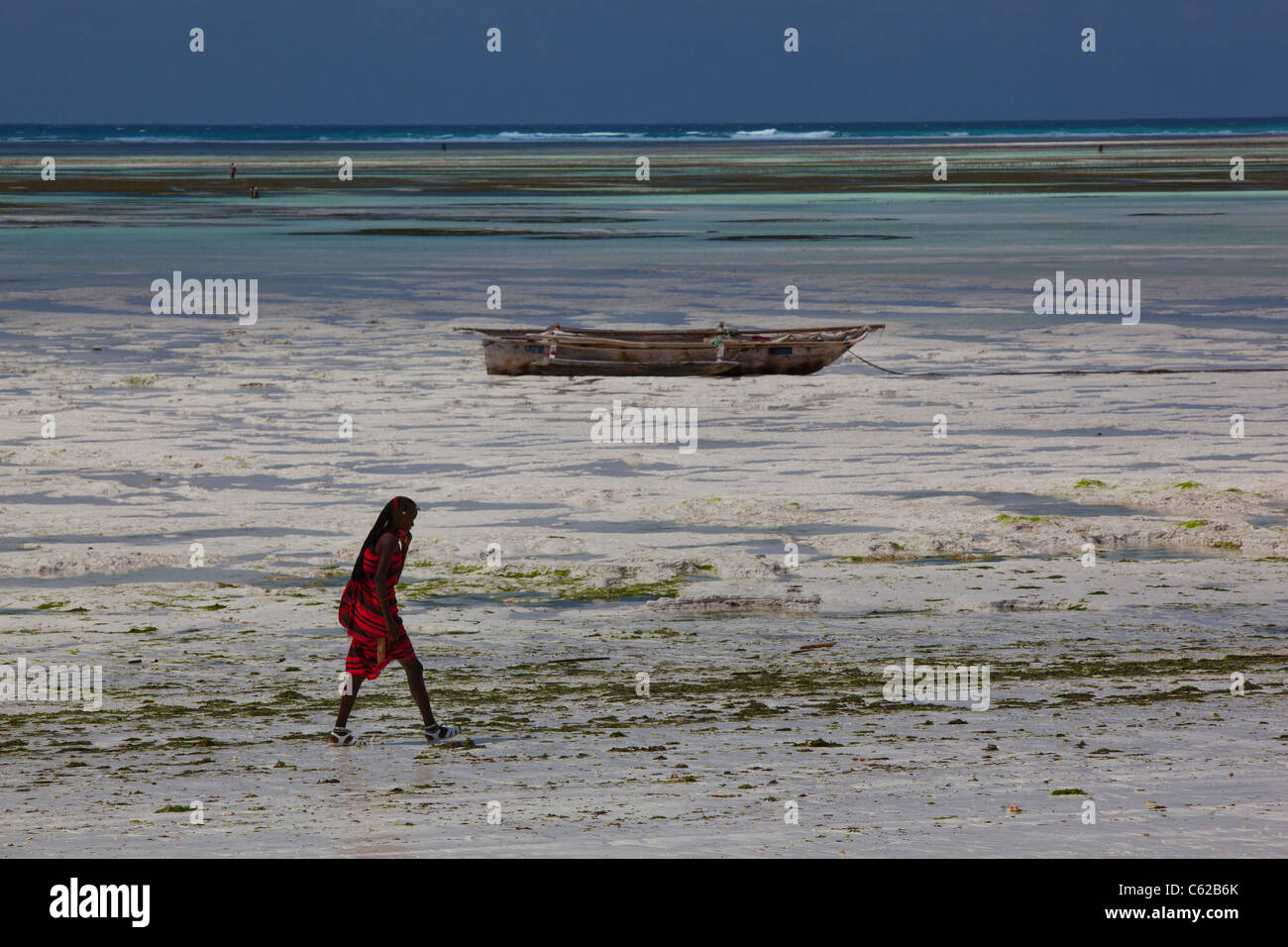 Un homme vêtu de vêtements Masai traditionnelle balade sur la plage de Zanzibar, Tanzanie. Banque D'Images Un homme vêtu de vêtements Masai traditionnelle balade sur la plage de Zanzibar, Tanzanie. Banque D'Images
