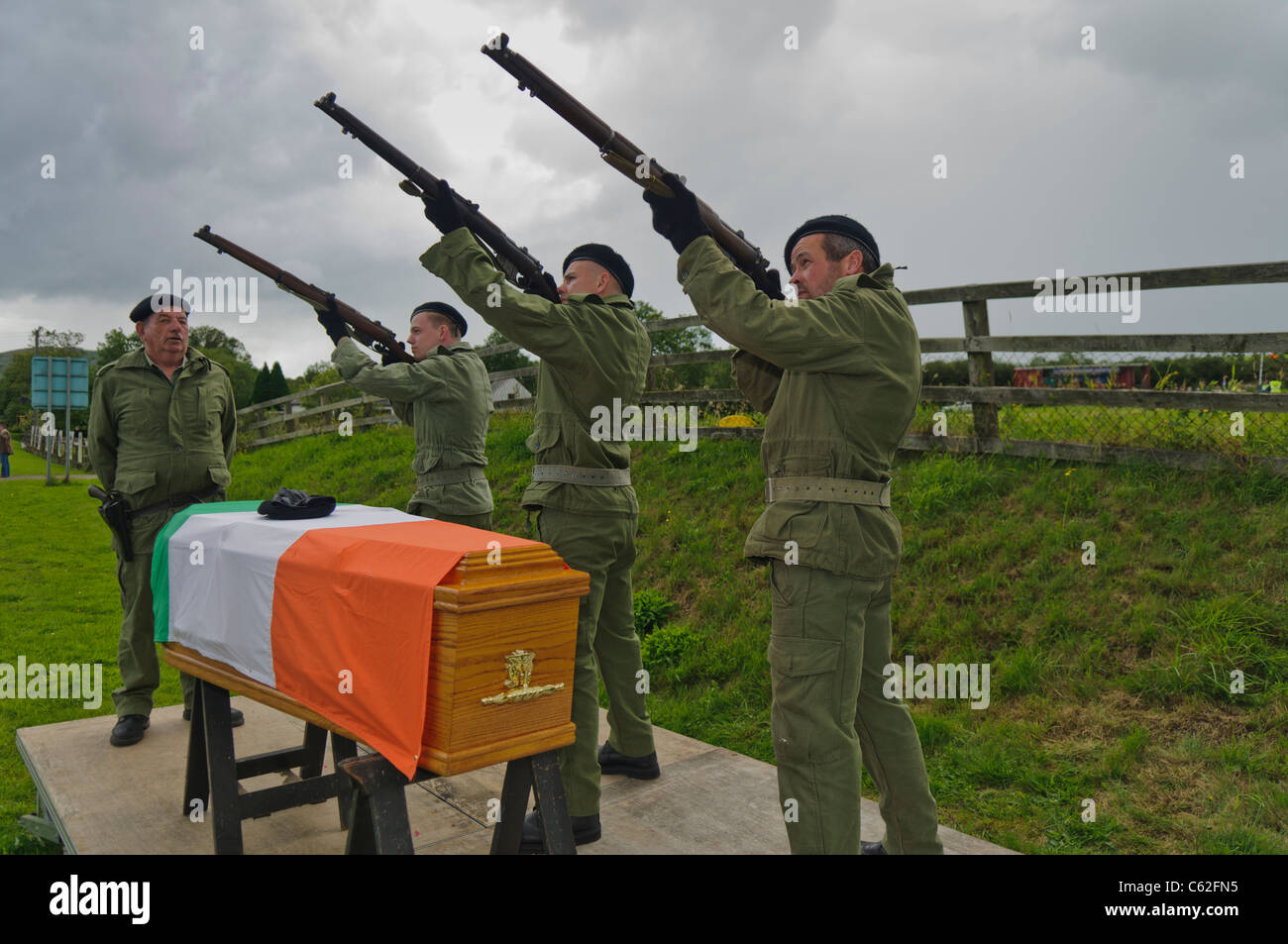 Des hommes vêtus d'uniformes paramilitaires de l'IRA au feu des fusils un cercueil drapé dans un drapeau tricolore irlandais Banque D'Images