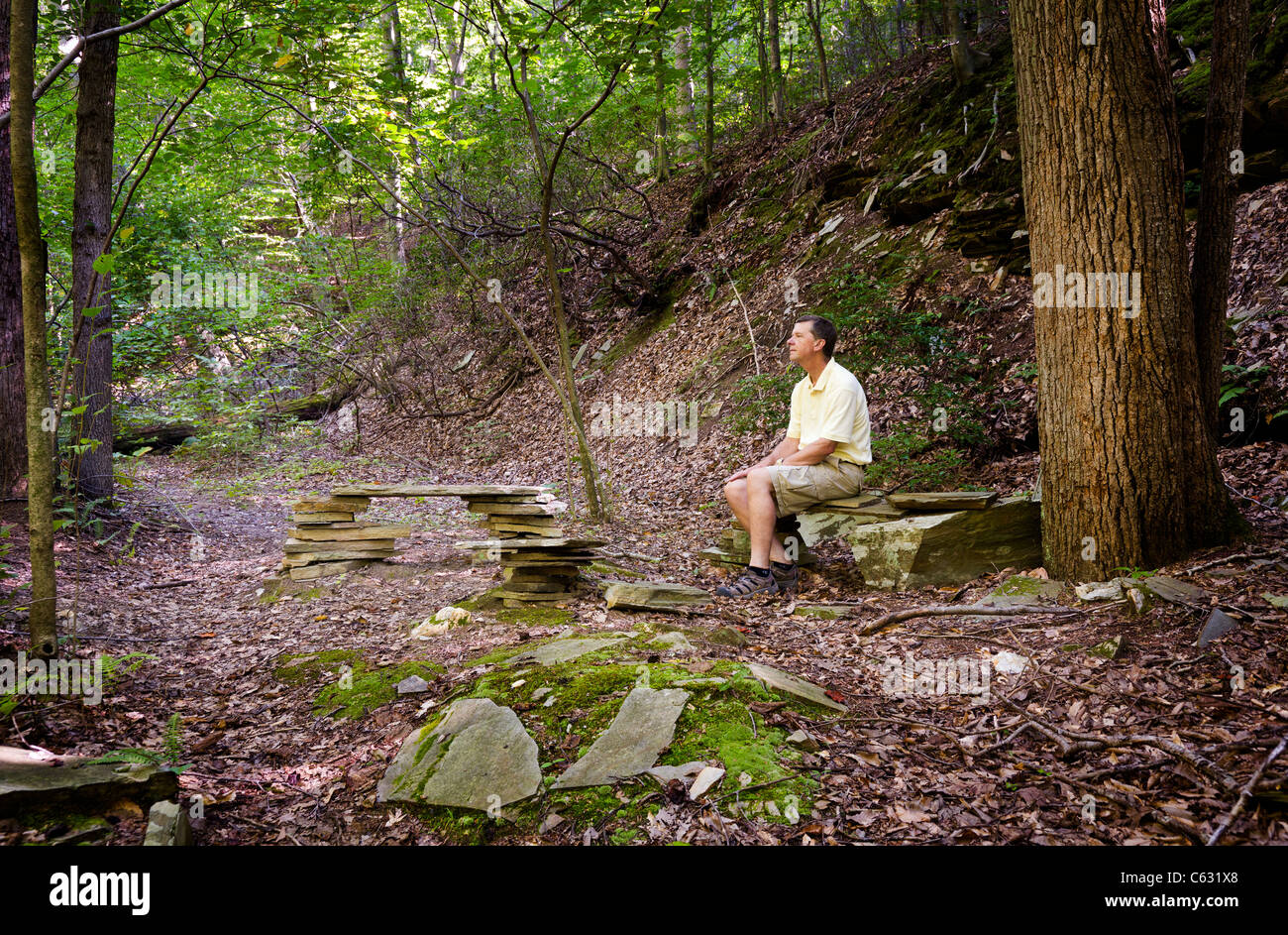 Randonneur à la retraite repose sur des bancs de pierre dans une clairière dans une forêt sur une randonnée Banque D'Images