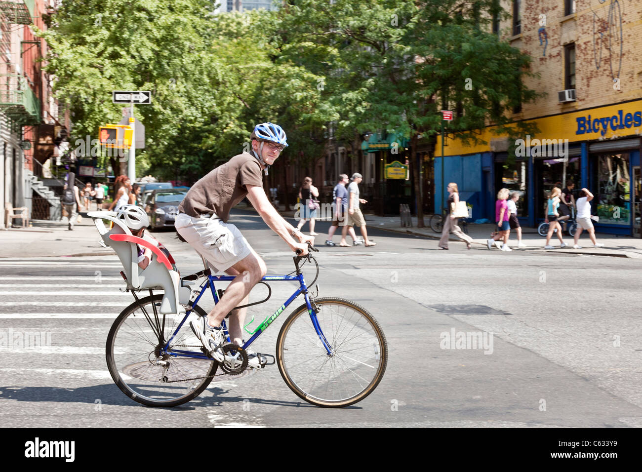 Cycliste avec tout-petit dans un siège pour enfant traverse une intersection sur 9e Avenue dans le quartier Hell's Kitchen à New York City Banque D'Images