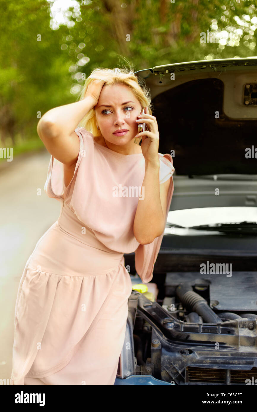 Photo de femme blonde dans la difficulté à rester debout par sa voiture et talking on cell phone Banque D'Images