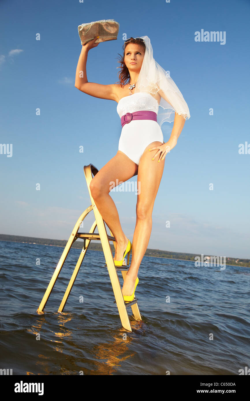 Belle Mariée slave debout sur l'escabeau en cour jaune chaussures. Bleu ciel et mer sur contexte. Banque D'Images