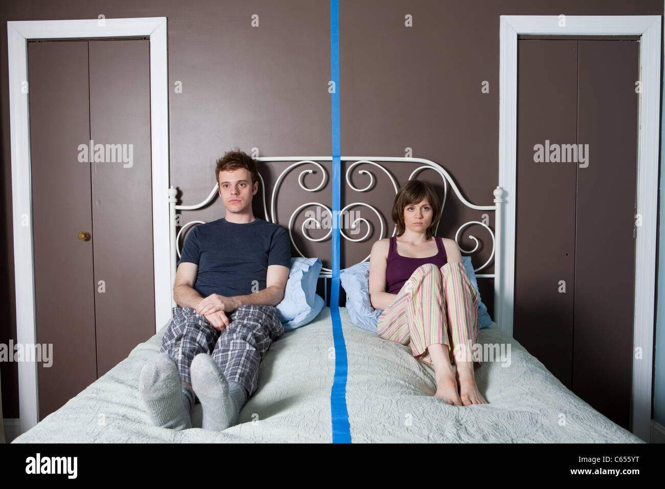 Young couple sitting on bed séparées par ligne bleue Banque D'Images