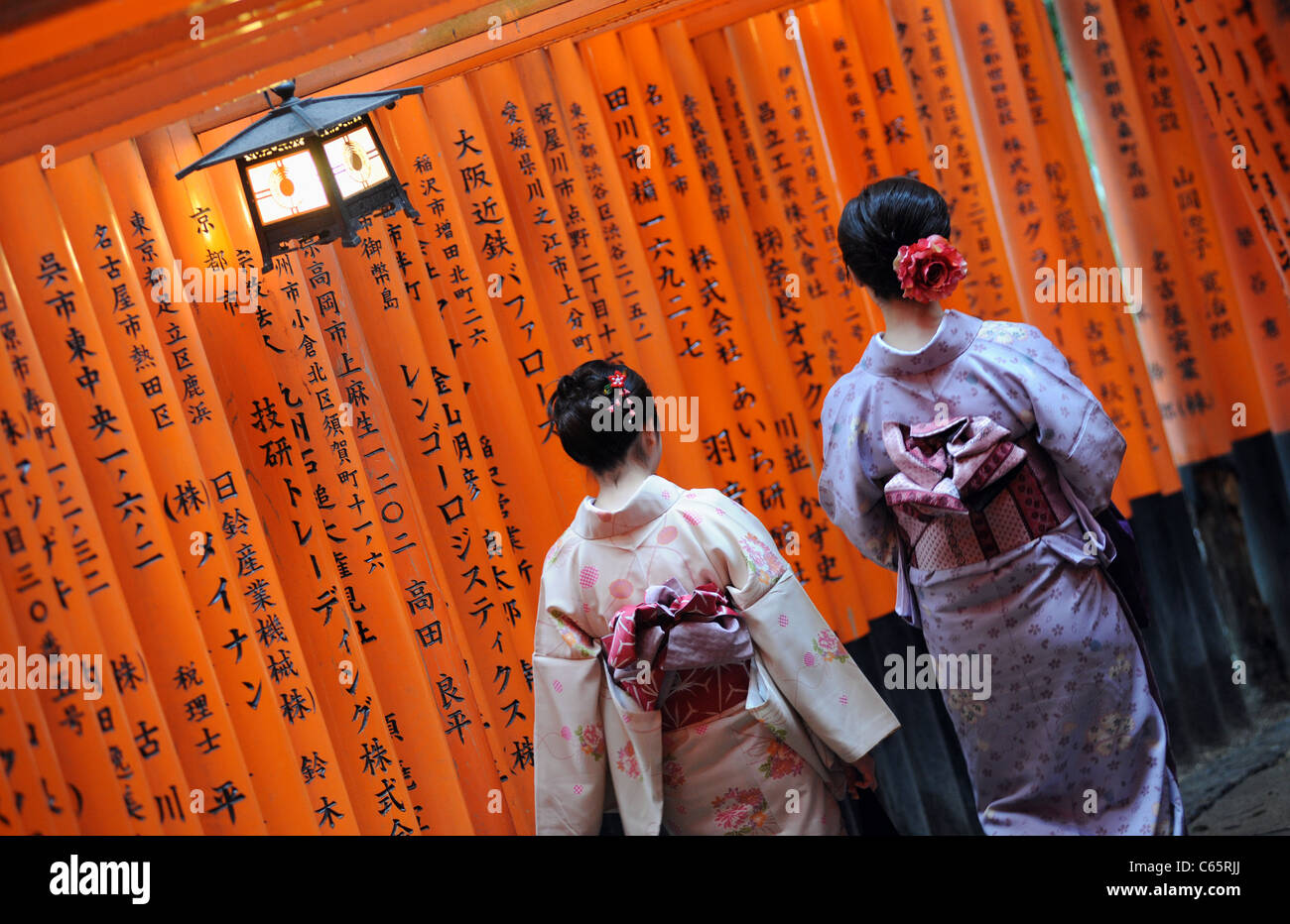 Deux femmes portant des kimonos japonais Torii passé à pied ou des portes rouges, doublure un chemin au Sanctuaire Fushimi Inari près de Kyoto. Banque D'Images