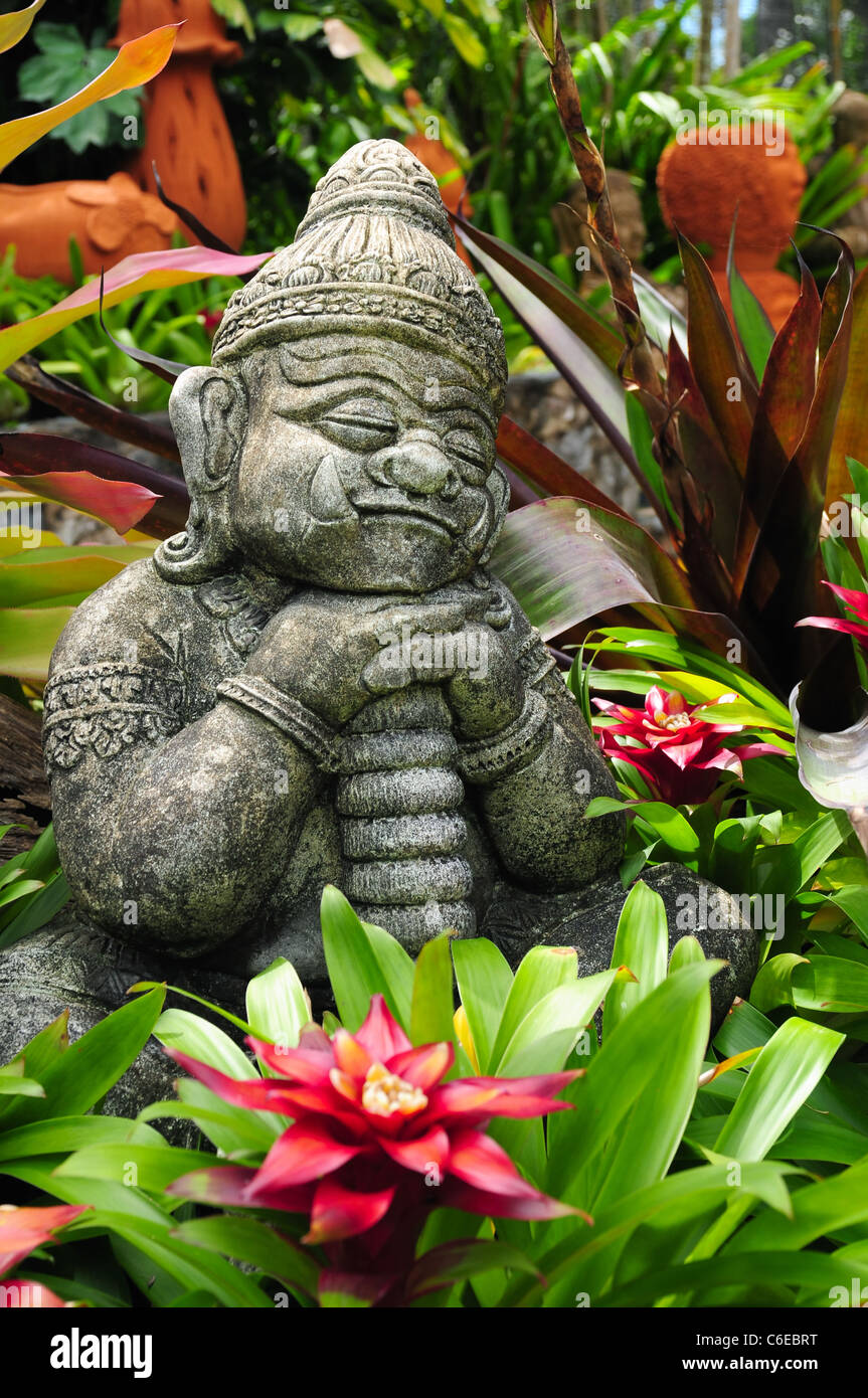 Statue de Bouddha - Portrait d'un coin couchage et souriant goblin entre plantes multicolores Banque D'Images