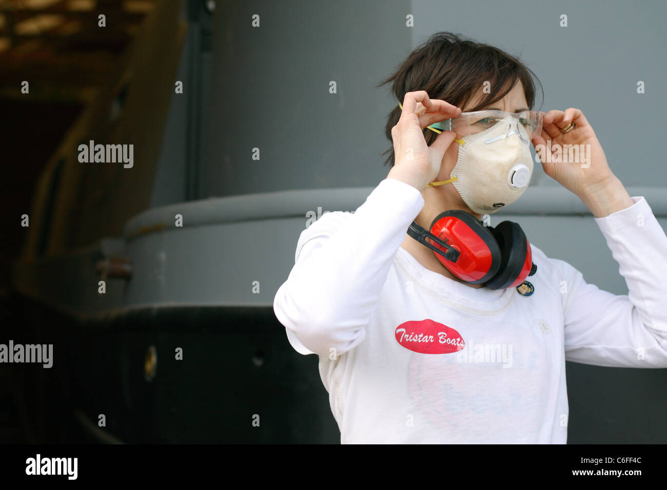 Une jeune femme de mettre un masque, protège-oreilles et des lunettes de protection lorsqu'il travaille. Banque D'Images